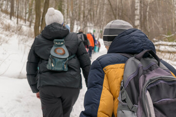 Fototapeta na wymiar People walk in winter through woods uphill. View from the back. Concept of travel, hiking, tourism.