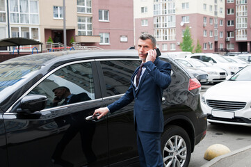 handsome male businessman in a suit stands next to a black car, concept of a successful business