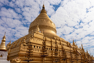 Fototapeta premium Shwezigon pagoda: golden buddhist temple, cloudy sky. Massive golden pagoda. Old Bagan, Myanmar, -Burma, Southeast Asia