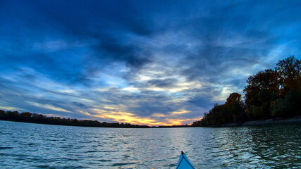 Meeting sunset on kayak. View from the bow of blue kayak to the river at sunset. Kayaking, canoeing, paddling