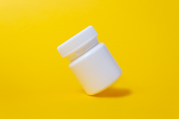 Whiteclosed plastic medicine jar. Vivid yellow background. Minimalistic medicine and healthcare concept. Pharmaceutical medicine. CLose up.