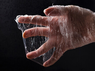 Human hand in the plastic sheeting against black background.Concept of global environmental...