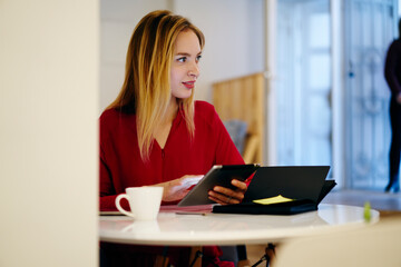 Pensive attractive blonde businesswoman checking email box via touchpad while planning working...