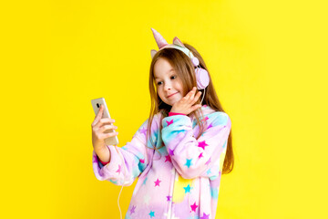 little girl in a unicorn costume takes a selfie. A child in a kigurumi unicorn smiles as he speaks on a video link against a yellow background.