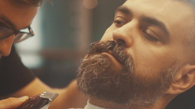 Barber shaving bearded man in barbershop. Male skin care and beard style concept. Close up of hipster male