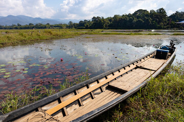 Boat floating on a lake with pink water lilies. Traditional burmese boat made of teak wood and covered in lacquer. Hills at the background. Editing space. Inle lake, Myanmar, Burma, south east Asia