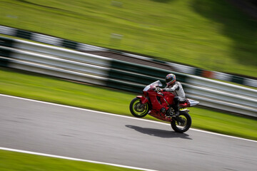 A panning shot of a red racing bike on one wheel as it circuits a track