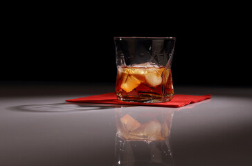 A glass of whiskey with ice on a red napkin and a dark background