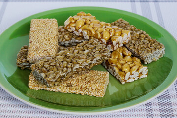 Kozinaki with seeds, nuts, sesame seeds and honey in a green plate. Useful snacks. Fitness diet food, nutritious snack, sesame halva, energy bar. Tasty and appetizing charge of energy. Close-up