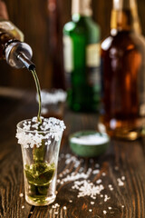 An alcoholic drink at the bar counter is poured into a tequila glass with salt at the edges, in the background are different bottles of alcohol, shallow depth of field, selective focus. The concept of