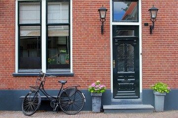Fototapeta na wymiar Front of traditional Dutch house with brick walls, steps, flower pots and black bike, Netherlands 