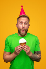 Funny male blowing candle on cupcake