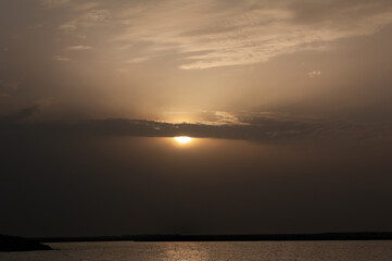 the sun peeks out from behind a cloud at sunset on the beach