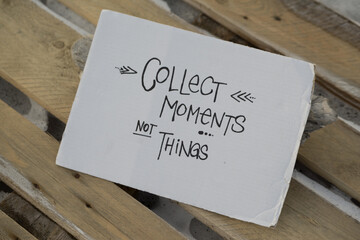 A piece of carton with the hand written words "collect moments not things". It is lying on a wooden palette with snow under it, on Spitsbergen.