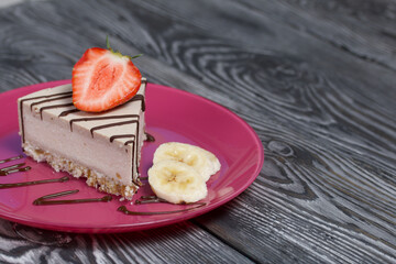 Cheesecake on a plate. Garnished with strawberries, bananas and chocolate. On brushed pine boards painted in black and white.