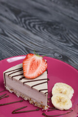 Cheesecake on a plate. Garnished with strawberries, bananas and chocolate. On brushed pine boards painted in black and white.