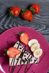 Cheesecake on a plate. Garnished with strawberries, bananas and chocolate. On brushed pine boards painted in black and white.