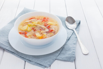 Fresh cabbage soup in white bowl and spoon on white wooden background with grey linen napkin. Bowl of traditional Russian shchi. Plate with soup
