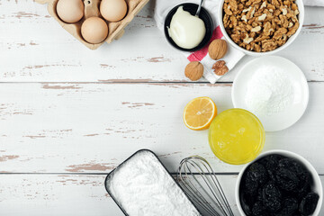 Ingredients for merengue roll cooking. Baking or cooking white wooden background with flour, sugar, eggs, egg white, prunes and walnuts.