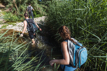 Small group of young tourists walking inside a river with little flow inside a forest in Spain in spring. Selective focus.