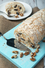 A piece of meringue roll with cake server and meringue roll on a white vintage wooden kitchen table with burlap napkin.