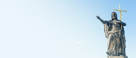 Banner with ancient statue of a saint monk with a cross at the Charles Bridge in Prague at blue sky and copy space for text, Czech Republic, summer, closeup
