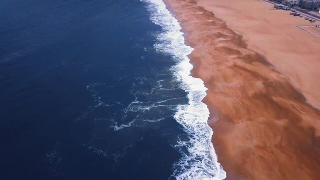 Flying over a sandy beach. Waves break on a sandy beach on the Atlantic coast, aerial View. Nazare, Portugal.