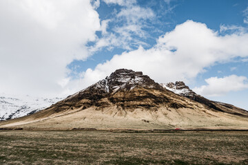Snow-covered peak rocky mountain covered with yellow dry grass in Iceland.