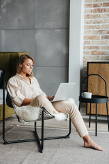 Image of nice woman working with laptop while sitting on armchair