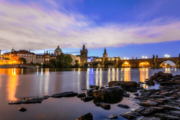 Towers and Charles bridge in the morning with moving clouds and stars. Stones on the foreground. Long exposure.