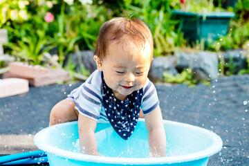 Fototapeta na wymiar 外で水色のタライで水遊びして大はしゃぎしている子供　ずぶ濡れの子供