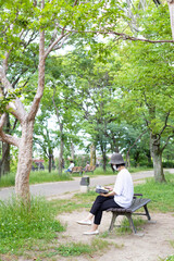Fototapeta premium 公園のベンチで帽子をかぶりマスクをして読書する1人の女性