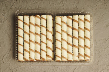 Sweet cookie straws in a plastic container on a gray table.