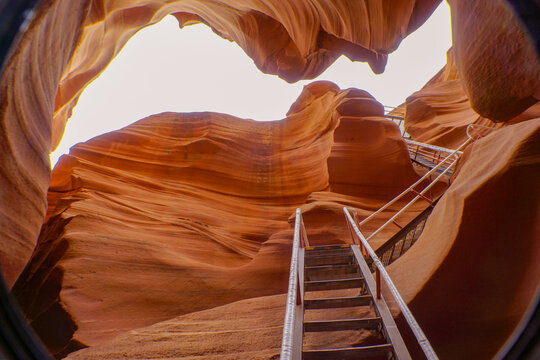 Worm's eye view of beautiful Lower Antelope canyon. A spectacular orange sandstone cave with white sky and metal stair at the entrance. Natural landscape