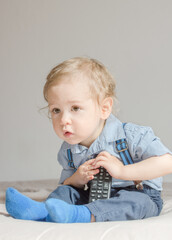 Cute baby boy playing with the remote control to watch TV sitting on a couch, at home