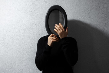 Dramatic portrait of young man with black oval mirror on face. Textured abstract background of grey...