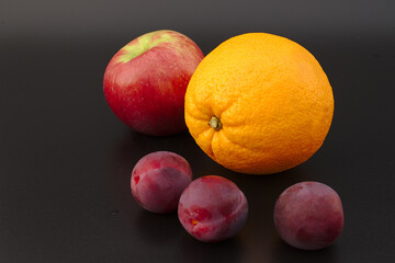 Orange, plum and apple on a black background. Close-up. Healthy eating concept.