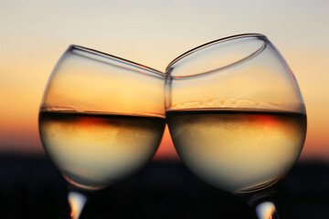 Two glasses with white wine on sunset background, evening sun is reflected in a misted glass. Concept of celebration, romantic evening at home quarantine, love date