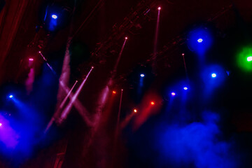 Fototapeta na wymiar Stage lights. Several projectors in the dark. Multi-colored light beams from the stage spotlights on the stage in the smoke at the time of the entertainment show. Night club. Lights show. Lazer show