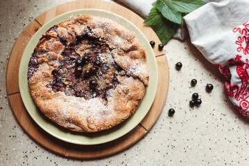 Realistic homemade blackcurrant pie on the kitchen table next to a linen apron and green leaves with berries. Top view.