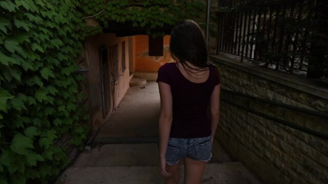 Young Caucasian woman wearing shorts walking down outside narrow cement steps, behind close up pan slow motion