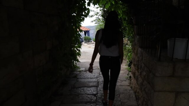 Young Caucasian Lebanese woman walking down steps inside tunnel and outside stone pathway, behind close up pan