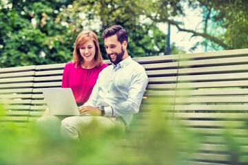 Portrait of businessman and businesswoman sitting on bench while working on laptop
