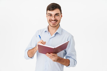 Photo of smiling handsome man in eyeglasses making notes in diary