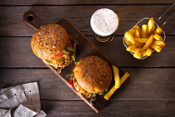 Beef burger in classic american style with hot grilled patty, melted cheese on top, tomato, onion, sauce and fried chips served with glass of beer. View from above, top view