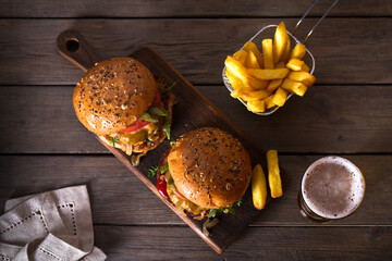 Beef burger in classic american style with hot grilled patty, melted cheese on top, tomato, onion, sauce and fried chips served with glass of beer. View from above, top view