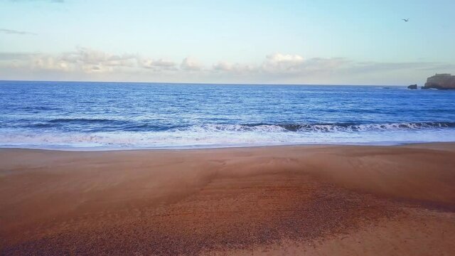 Flying over a sandy beach. Waves break on a sandy beach on the Atlantic coast, aerial View. Nazare, Portugal.
