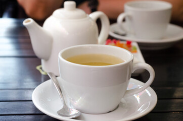 Two white cups of herbal tea. Set with teapot on a dark wooden table.