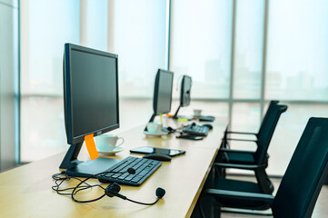 Customer support representative talking on headset while using computer. Businessman working at desk with colleague in background. He is wearing casuals in call center.