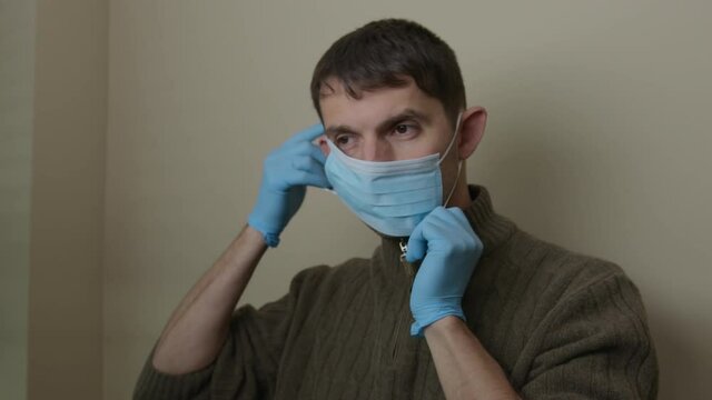 High quality close-up 4k slow motion video of a man wearing blue rubber protective medical gloves and blue medical face mask indoor to protect himself from the epidemic. COVID 19 self-protection. 